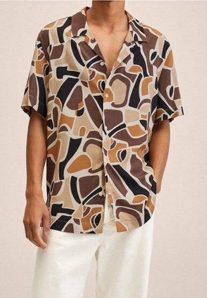 Homme portant une chemise à manches courtes à boutons avec un motif géométrique abstrait marron, beige, noir et fauve et un pantalon blanc.