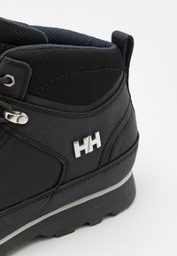 Bota de senderismo negra con parte superior texturizada, acento de logo plateado, cuello acolchado y suela resistente. Las características incluyen sistema de cordones y material duradero.