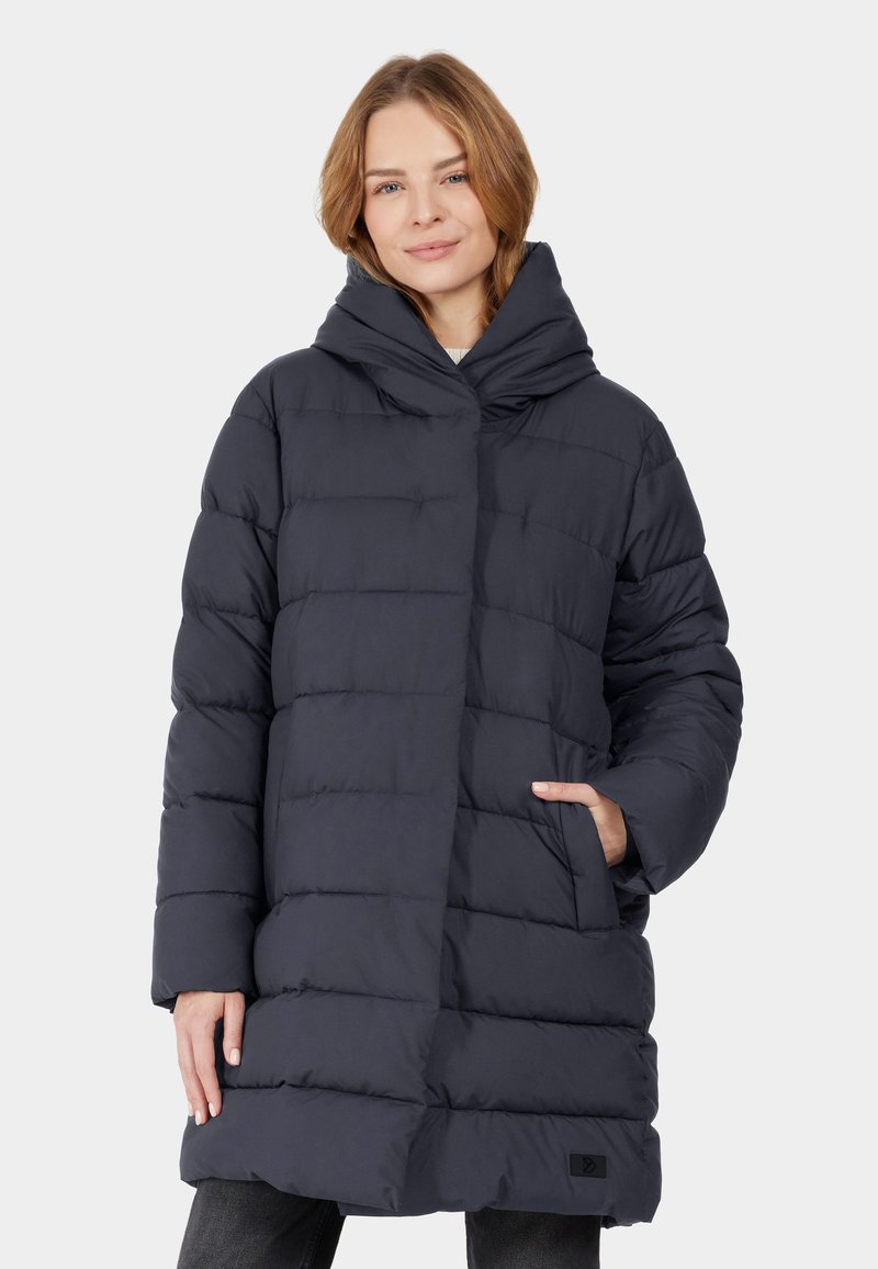 Puffer coat in dark navy with a high collar, oversized hood, and vertical quilted texture. Features side pockets and a subtly branded accent.