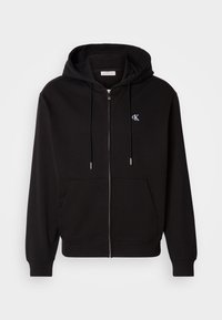 Sweat à capuche noir zippé avec poches avant, capuche à cordon, poignets côtelés et petit logo blanc "cK" sur le côté gauche de la poitrine.