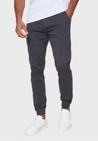 Gray, tapered jogger pants with elastic cuffs and side pockets, made from cotton-blend fabric, paired with white sneakers.