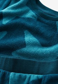 Fleece-Sweatshirt in dunklem Türkis mit helleren Türkis-Akzenten. Ausgestattet mit einem gerippten Rundhalsausschnitt und einer weichen, strukturierten Oberfläche. Abstraktes Muster vorhanden.