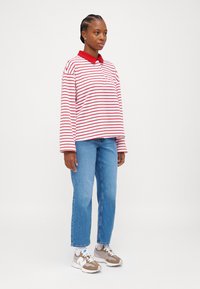 Red and white striped long-sleeve polo shirt with collar, paired with light blue straight-leg jeans and beige sneakers.