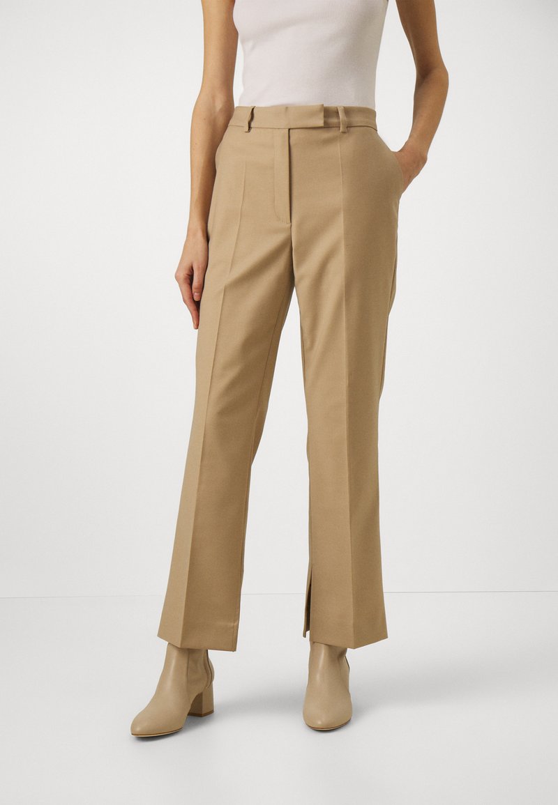 Høyt midje beige bukser med rett ben, som har sidelommer, beltehemper og elegant skreddersøm, kombinert med beige ankelstøvler.