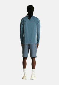 Blaues sportliches Langarmshirt mit Raglanärmeln, kombiniert mit passenden Shorts. Das Outfit zeichnet sich durch eine glatte Textur und minimale Details aus.
