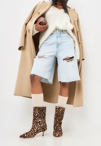 Lichtblauwe gescheurde denimshorts, romige gebreide trui, beige jas, tan sokken en bruine enkellaarsjes met luipaardprint en een spitse neus.