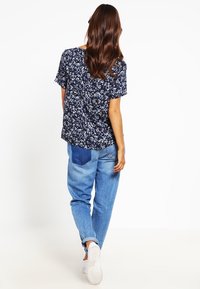 Marinblommig kortärmad topp som kombineras med ljusblå denimjeans med ett lapptäcke. Vita sneakers fulländar outfiten.