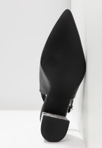 Vue de dessous d'une chaussure noire à bout pointu avec un talon bloc et une semelle lisse sur fond blanc.