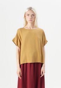 Kortskaftet sennepsgult bluse med en avslappet passform og bred halslinning, paret med et langt bordeauxfarget skjørt. Glatt tekstur, minimalistisk design.