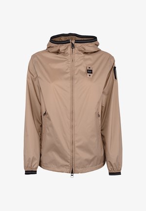 Giacca beige leggera con cappuccio, zip frontale, due tasche laterali con zip, polsini elasticizzati e toppe con logo nero sul petto e sulla manica.