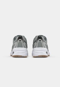 Scarpe da ginnastica grigie con tomaia in rete, suola in gomma e intersuola bianca. Presentano dettagli neri e un design del tacco arrotondato.
