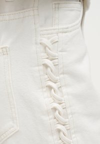 Κοντινή λήψη λευκού υφάσματος τζιν με λεπτομέρεια πλεκτού σχοινιού που τρέχει κάθετα κατά μήκος των ραμμένων ραφών.