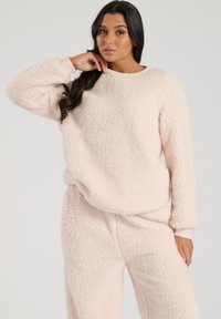 Light pink fleece loungewear set with a soft, textured finish. The top features a round neck and long sleeves, complemented by elastic cuffs.