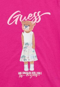 Ροζ μπλουζάκι με γραφικό αρκούδας σε λευκό τοπ και ανοιχτό μπλε φούστα με σχέδιο φοινικόδεντρων. Το κείμενο γράφει "Guess" και "Los Angeles Est. 1981."