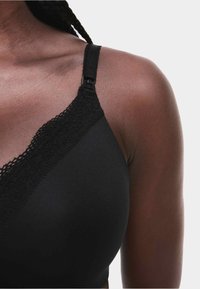 Soutien-gorge noir en tissu doux avec une bordure en dentelle le long du décolleté. Bretelle réglable avec une fermeture métallique et texture lisse. Vue en gros plan.