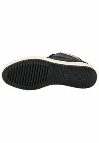Černá gumová podrážka tenisky s rýhovaným povrchem, obsahující malé ventilační otvory a logo vyražené na patě. Světlé detaily na okrajích.