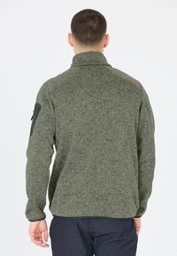 Fleece-tröja, mörkgrön med texturerad yta, hög krage och svarta axeldetaljer. Har en ficka med dragkedja på ärmen.