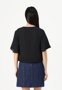 Svart kortärmad topp med en rosa krage, tillsammans med en blå denimkjol med vertikala ränder och en detalj med dragkedja fram.