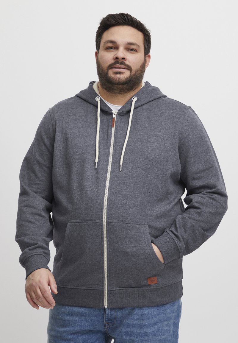 Felpa grigia con zip realizzata in tessuto morbido, caratterizzata da una chiusura frontale a zip, ampie tasche, cappuccio con cordino e dettaglio in pelle sull'orlo.