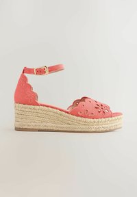 Sandale compensée rose corail avec bride à la cheville, bord festonné, détails ajourés floraux et semelle plateforme en jute tressée.