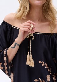 Czarna bluzka bez ramiączek z kwiatowym haftem, z plecionym wiązaniem z frędzlami i szerokimi rękawami. Gładka tekstura materiału.