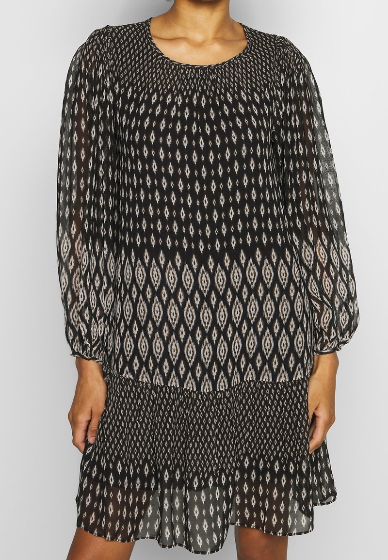 Svart långärmad klänning i lätt, genomskinligt tyg med ett diamantmönster i beige och vitt, med samlad halsringning och lager-på-lager nederdel.