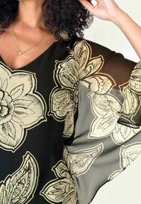 Blusa negra con estampado floral en crema, de corte holgado, escote en V y mangas amplias y fluidas. Material translúcido con textura suave.