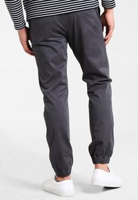 Joggers gris élastiqués avec une coupe fuselée, réalisés en tissu doux. Ils disposent d'une taille à cordon de serrage et de chevilles resserrées, associés à des baskets blanches.