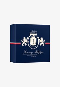 Granatowe pudełko z grafiką białego lwa i korony, z napisem "IMPACT" oraz "Tommy Hilfiger" w stylowej typografii i akcentem czerwonego paska.