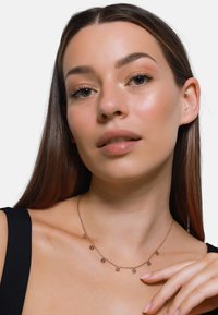 Goldene Halskette mit sonnenförmigen Anhängern, die ein filigranes Design aufweist. Das Model trägt ein schwarzes Oberteil mit einem glatten, gleichmäßigen Ausschnitt.