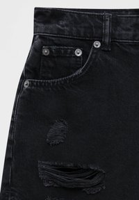 Vaqueros de mezclilla negra con cintura alta, con detalles desgastados en la pierna, herrajes plateados y una tela suave y texturizada.