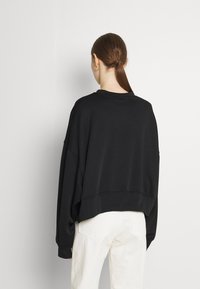 Svart oversize-tröja med rund halsringning och nedhasade axlar, med ett strukturerat tyg. Bärs med vita byxor och visar en avslappnad passform.