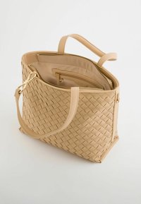 Beige vævet tote taske med dobbelte håndtag, tekstureret overflade, guldhardware og en indvendig lynlåslomme til sikker opbevaring.