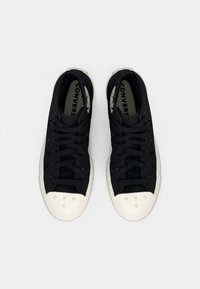 Schwarze Canvas-Sneaker mit einer weißen Gummikappe, ausgestattet mit schwarzen Schnürsenkeln, strukturierten Seitenpaneelen und Branding auf der Zunge.