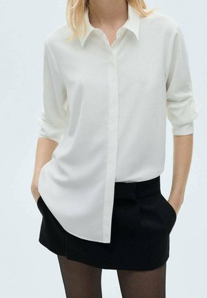 Witte blouse met lange mouwen, voorzijde met knopen, losse pasvorm en opgerolde mouwen, gecombineerd met een zwarte rok met hoge taille.