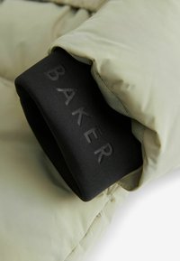 Puffjakke i lysegrøn med sort elastisk manchette med prægning af "BAKER" branding. Glat tekstur og quiltede stofs detaljer.