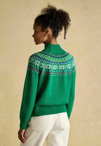 Grüner gestrickter Pullover mit hohem, geripptem Kragen. Verfügt über bunte geometrische Muster an der Passe sowie gerippte Bündchen und Saum.