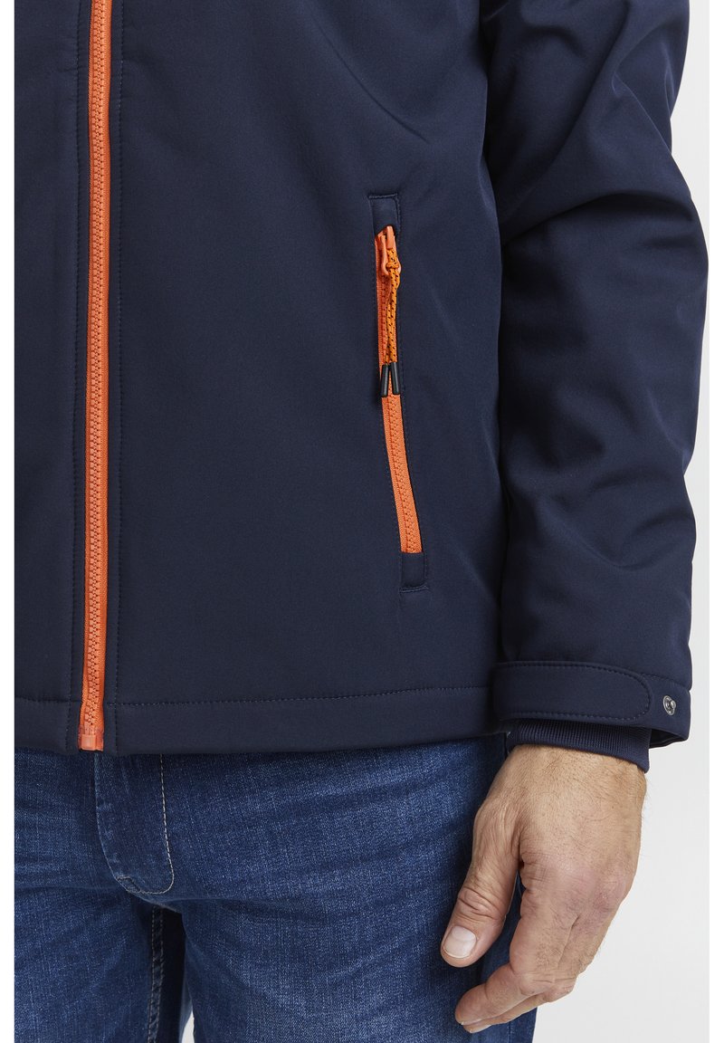 Giacca navy con cerniere arancioni, inclusa una tasca sul petto. Presenta una trama liscia, polsini elasticizzati e una vestibilità aderente.