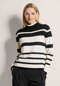 Gestreifter Pullover in Schwarz und Weiß mit hohem, geripptem Kragen und gerippten Bündchen, aus weichem Strickmaterial. Lockere Passform.
