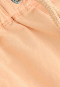 Tissu de couleur pêche avec une texture douce, présentant une taille froncée et un cordon de serrage. Des coutures sont visibles le long des bords.