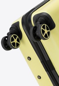 Valigia rigida di colore giallo chiaro, con cerniera nera e dettagli in nero. Quattro ruote multidirezionali per una facile manovrabilità.