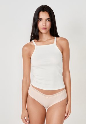 Camiseta blanca con ligeras costillas y tirantes finos, combinada con panty nude con encaje en la cinturilla y los aberturas de las piernas.