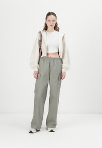 Grijze cargobroek met elastische tailleband, twee zijzakken; gecombineerd met een cropped witte top en een oversized crèmekleurige hoodie. Neutrale sneakers.