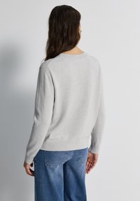 Lichtgrijze gebreide trui met een ronde halslijn, geribbelde mouwen en onderrand. Zachte textuur, klassieke pasvorm en eenvoudig ontwerp. Gepaard met blauwe jeans.