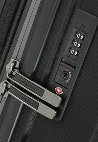 Schwarze Hartschalenreisetasche im Close-up mit doppelt silbernen Reißverschlüssen, Kombinationsschloss und TSA-zugelassenem Schlüsselloch. Estrukturierte Oberfläche für Langlebigkeit.
