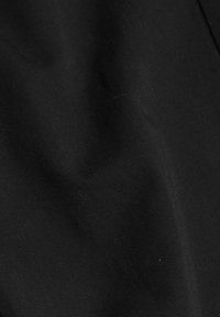 Svart tyg med subtil diagonalkonstruktion och mjuka veck som skapar ljus- och skuggeffekter.