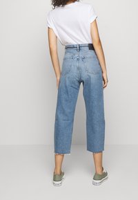 Džíny s vysokým pasem, světle modré, rovný střih, s neopracovaným lemem a zadními kapsami, nošeny s bílým tričkem a zelenými teniskami.