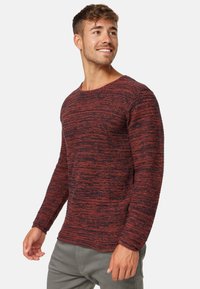 Czerwony i ciemnoszary sweter w paski z długimi rękawami, okrągłym dekoltem i teksturowanym materiałem, noszony z szarymi spodniami. Miękki, casualowy design.