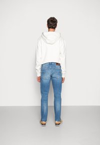 Vit kortärmad hoodie med huva, i kombination med ljusblå denimjeans med en slät textur och minimal blekning, bärs med bruna skor.