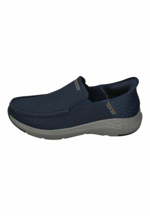 Zapatos de hombre tipo slip-on en color navy, con parte superior de tela texturizada, suela de goma gris y detalles sutiles. Cuentan con un cuello acolchado y paneles laterales elásticos para mayor comodidad.
